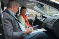 Ein Mann und eine Frau sitzen in einem parkenden Auto und unterhalten sich