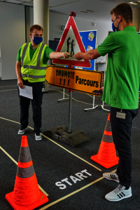 Foto: Zwei Auszubildenden der BASF Digital Solutions GmbH reichen sich einen Zettel zu, dahinter steht ein Schild mit der Aufschrift "Smombie-Parcours"
